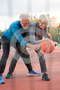 Cheerful active senior couple playing basketball on the urban basketball street court