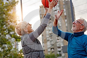 Cheerful active senior couple playing basketball on the urban basketball street court
