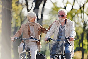 Cheerful active senior couple riding bicycles in public park together having fun. Perfect activities for elderly people.