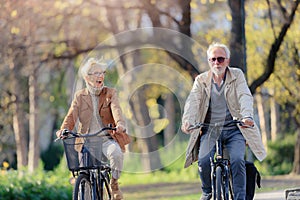 Cheerful active senior couple riding bicycles in public park together having fun. Perfect activities for elderly people.