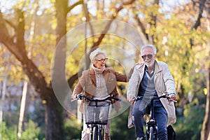 Cheerful active senior couple riding bicycles in public park together having fun. Perfect activities for elderly people.