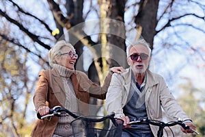 Cheerful active senior couple riding bicycles in public park together having fun. Perfect activities for elderly people.