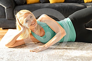 Cheerful and active senior woman doing stretching exercise at home. Grandmother in sportswear warming up and doing