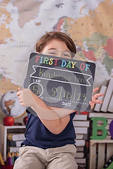 Cheerful adolescent boy holding a chalkboard sign for the first day of kindergarten