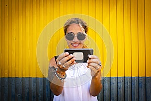 Cheerful adult beautiful woman taking selfie picture with modern phone and urban yellow and blue background - modern people