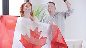 Cheerful adult couple holding Canadian flag talking looking at camera. Positive redhead woman and brunette man posing