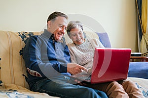 Cheerful adult couple sitting on a couch and watching a program on a laptop. selective focus photo