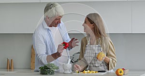 Cheerful adult daughter and happy senior father preparing healthy food