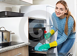 Cheerful adult girl in gloves removing oven