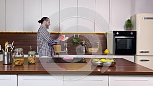 Cheerful adult man washing dishes with washcloth detergent at home