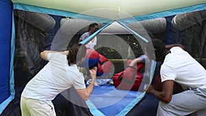 Cheerful adult women in big boxing gloves having fun on inflatable ring in outdoor amusement park