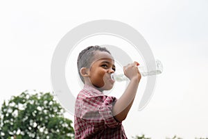 Cheerful african american boy drinking water after playing at park