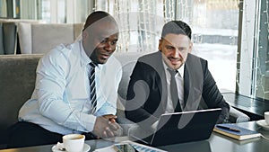 Cheerful African American businessman in formal clothes discussing business project with his caucasian colleague on his