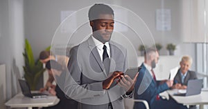 Cheerful african-american businessman using tablet computer standing in modern office