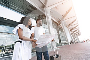 Cheerful african american couple searching map at airport building