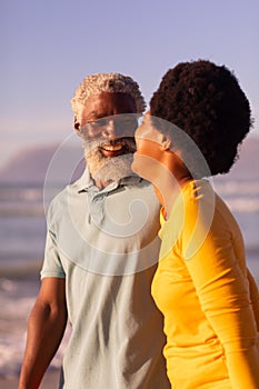 Cheerful african american couple talking while standing at beach and clear blue sky at sunset