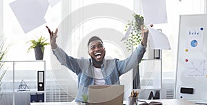 Cheerful african american employee celebrating success throwing papers in office