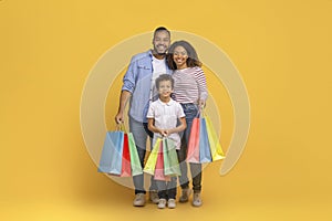 Cheerful african american family holding shopping bags, standing together with joyful expressions