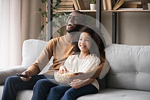 Cheerful african american father and child girl laughing watching tv