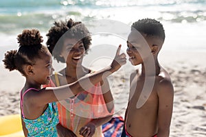 Cheerful african american girl applying suntan lotion on brother's nose by mother at beach