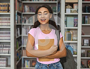 Cheerful african american girl student standing between bookshelves