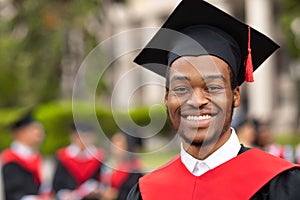 Cheerful african american guy in graduation costume, closeup portrait