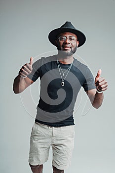 Cheerful african american guy in a hat and summer clothes raises thumbs up and smiles