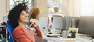 Cheerful african-american guy talking on phone at workplace
