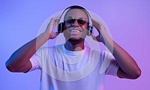 Cheerful African American Guy In Wireless Headphones And Sunglasses In Neon Light