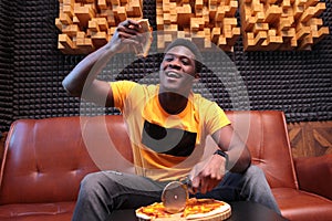 The cheerful African-American held up a slice of pizza. Photo in the interior. The concept of a good mood. Copy of the