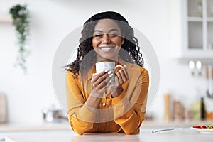 Cheerful african american lady drinking tea at home