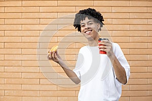 Cheerful African-American man holding a cup of coffee and an orange donut