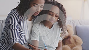 Cheerful african american mother helping her daughter to do homework, writing together in copybooks, tracking shot