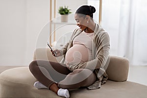 Cheerful african american pregnant woman using phone at home