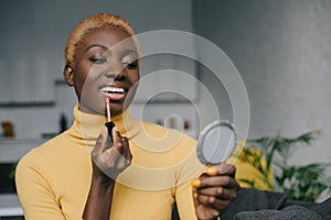 Cheerful african american woman applying lip gloss and looking photo