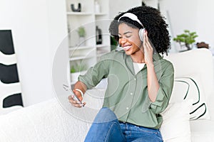 A cheerful African-American woman with headphones is sitting comfortably on a sofa