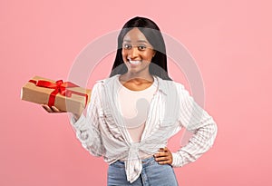 Cheerful African American woman with holiday gift box on pink studio background