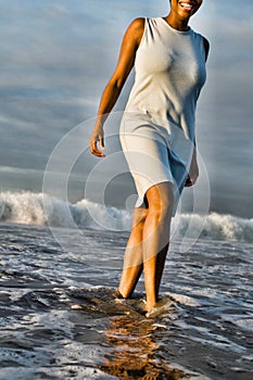 Cheerful African American woman walking through surf on beach