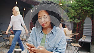 Cheerful African American woman wearing earphones while holding her smartphone. Young female listening music while