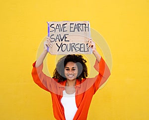 Cheerful African American young woman holding a sign that says: Save earth save yourself. Environmentalism, not planet b