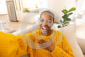 Cheerful african american young woman screaming and gesturing while taking selfie on sofa