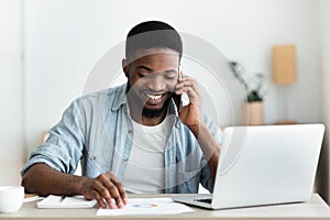 Cheerful african businessman checking financial reports and talking on phone