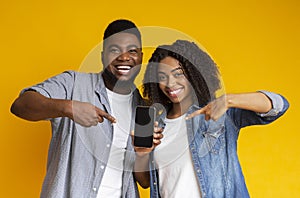 Cheerful african couple pointing at smartphone with black screen for mockup