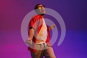 Cheerful african guy dancing  over purple neon background