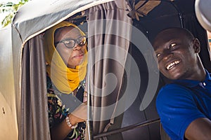 cheerful african man driving a auto rickshaw taxi smiling while listening to a female passenger who& x27;s talking to him