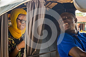 cheerful african man driving a auto rickshaw taxi smiling while listening to a female passenger who& x27;s talking to him