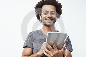Cheerful african man in headphones smiling holding tablet looking at camera. White background.