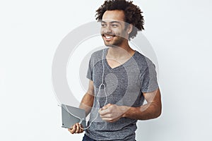 Cheerful african man in headphones smiling holding tablet over white background.