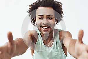 Cheerful african man in headphones smiling stretching hands to camera. White background.