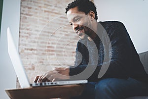 Cheerful African man using computer and smiling while sitting on the sofa.Concept of young business people working at